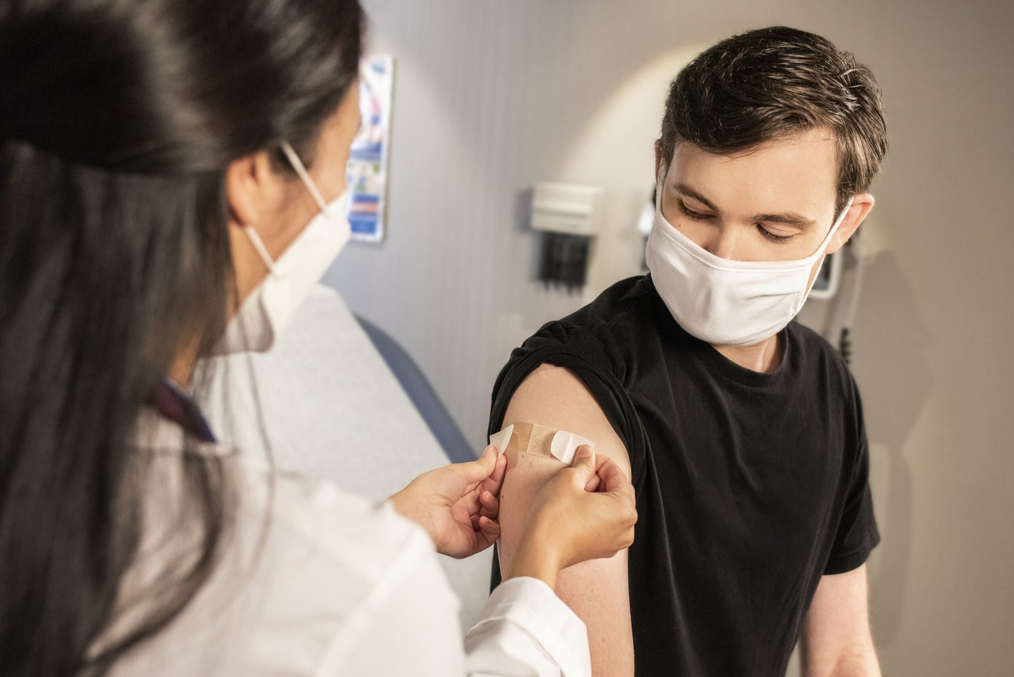 Young person receiving vaccine from healthcare worker while wearing a mask.