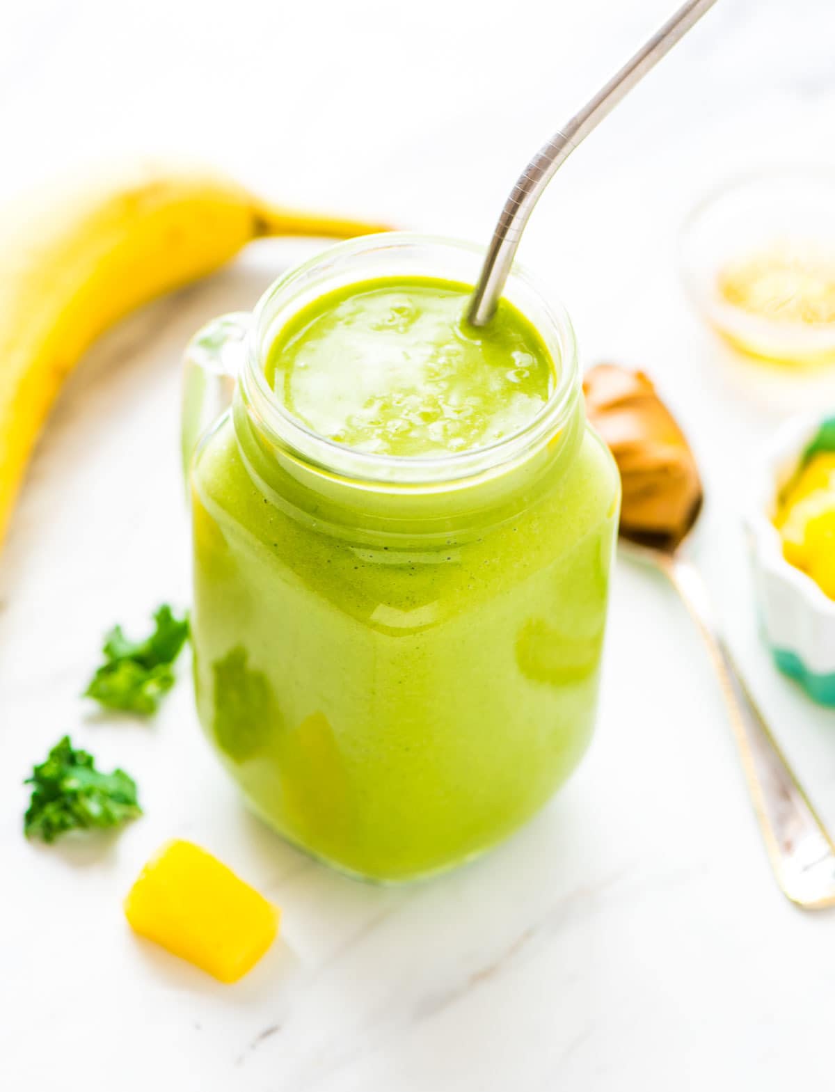 Good for you kale smoothie in a glass made with ingredients like bananas, pineapple, and honey which have tons of health benefits